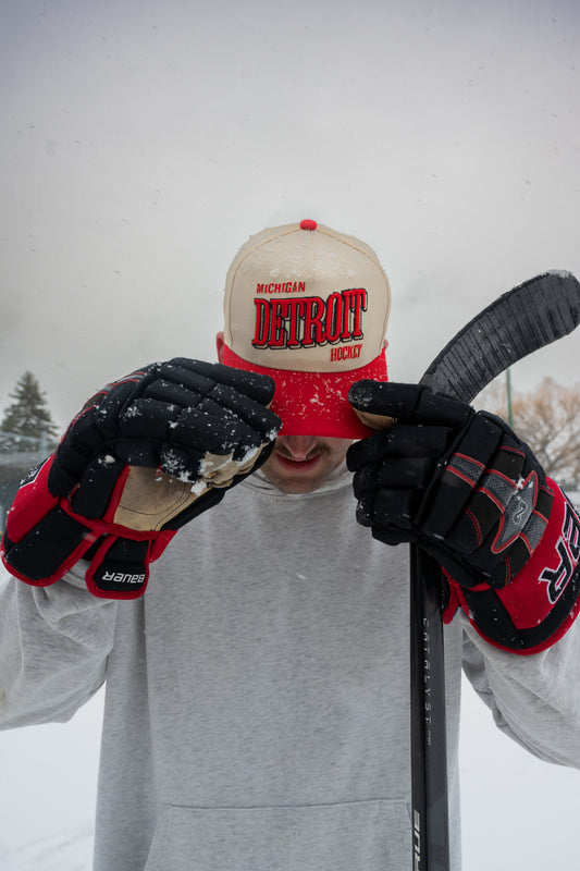 Person wearing Outland Club Co. Detroit City Ice Classic Snapback Hat outdoors in snow with hockey gloves and stick, Michigan hockey lifestyle shot